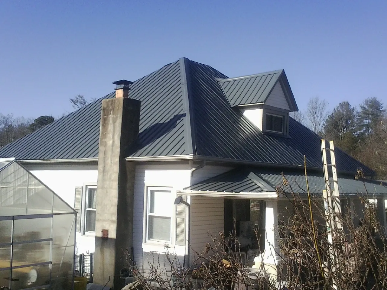 Dark blue standing seam metal roof on a white farmhouse with dormer — Slate & Tile Roof Repair by Roofing Brothers in Clearbrook