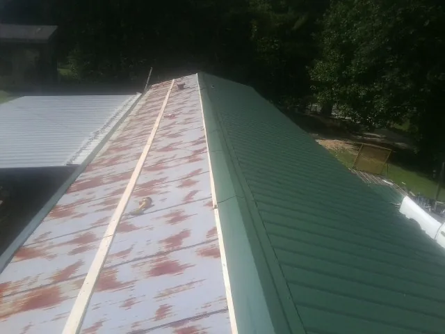 Old rusted panels beside newly installed green metal roofing — Wind Damage Roof Repair by Roofing Brothers in Clearbrook