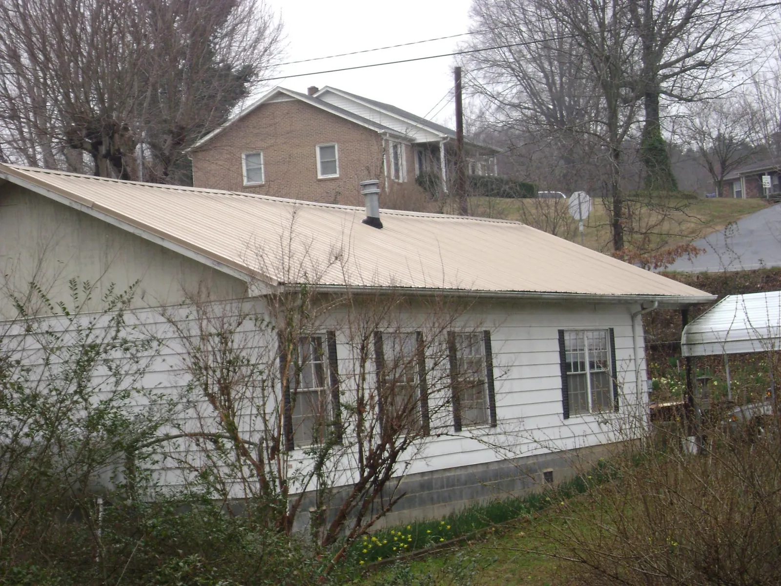 Tan metal roof on a white sided house set into a hillside — Commercial Roofing by Roofing Brothers in Clearbrook