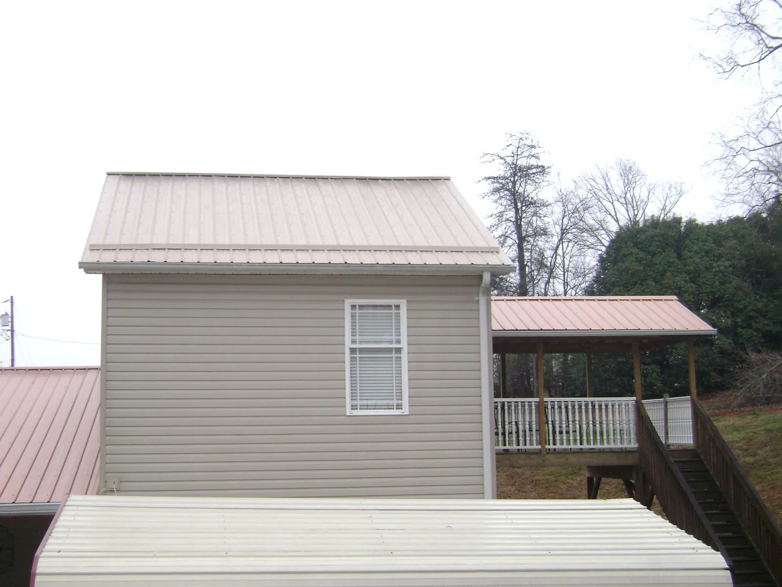 Tan metal roofs on a two story addition and attached porch, from a Roof Replacement job in Clearbrook